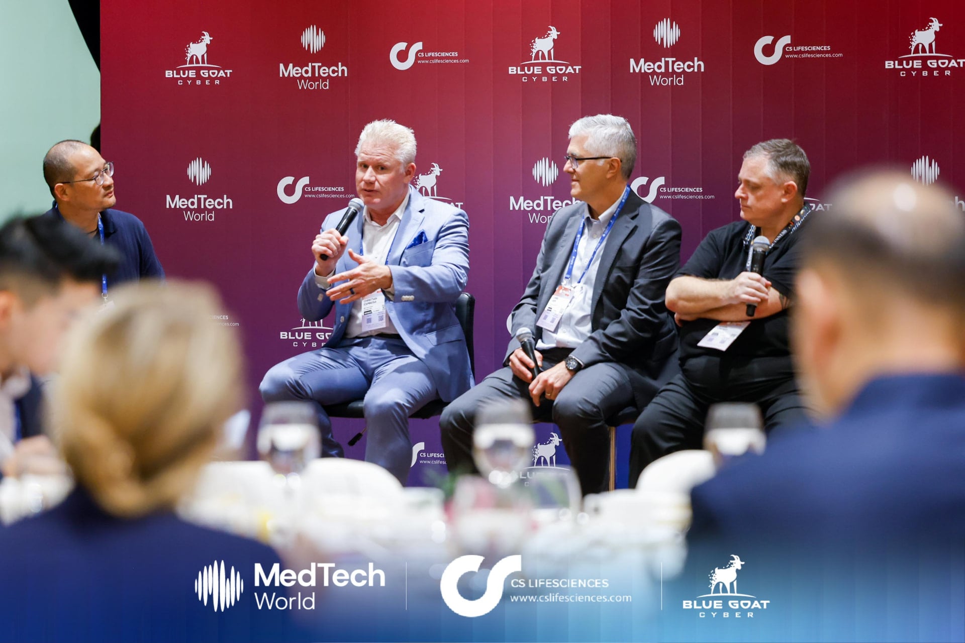 Christian Espinosa on a four-person panel in front of the Blue Goat Cyber and MedTech World backdrop at the MedTech World Asia luncheon