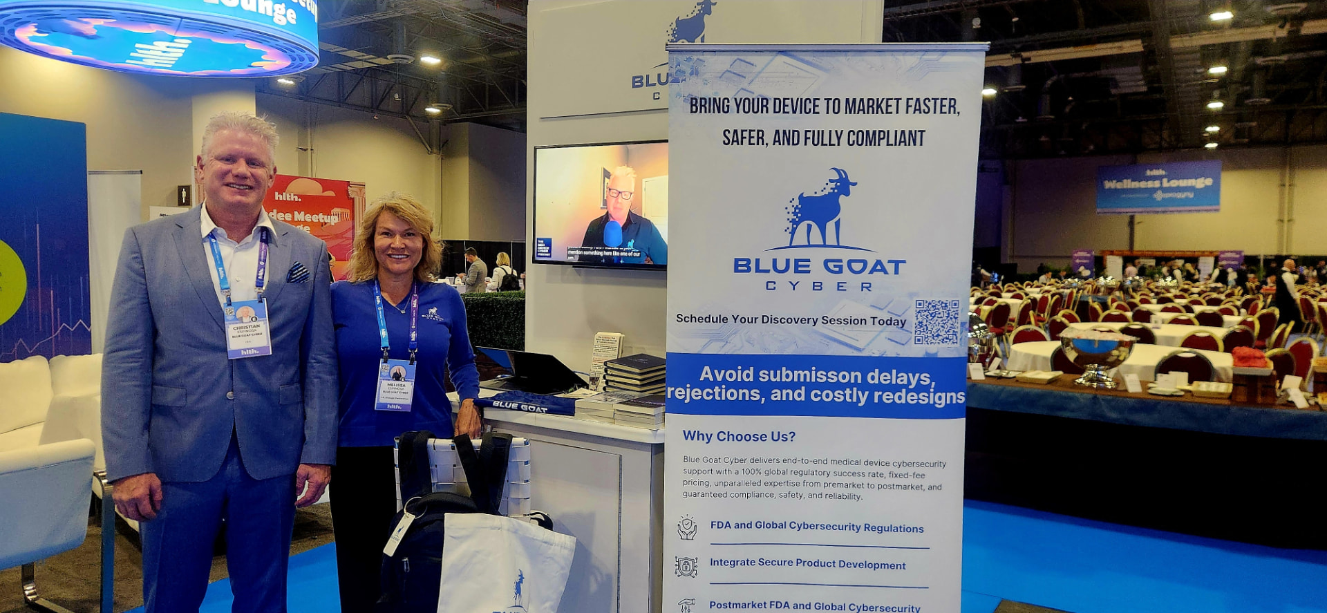 Christian and Melissa Espinosa standing beside the Blue Goat Cyber banner at the HLTH conference