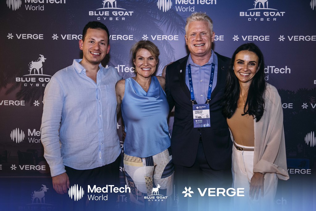 Christian Espinosa with three partners in front of the Blue Goat Cyber, MedTech World, and Verge backdrop